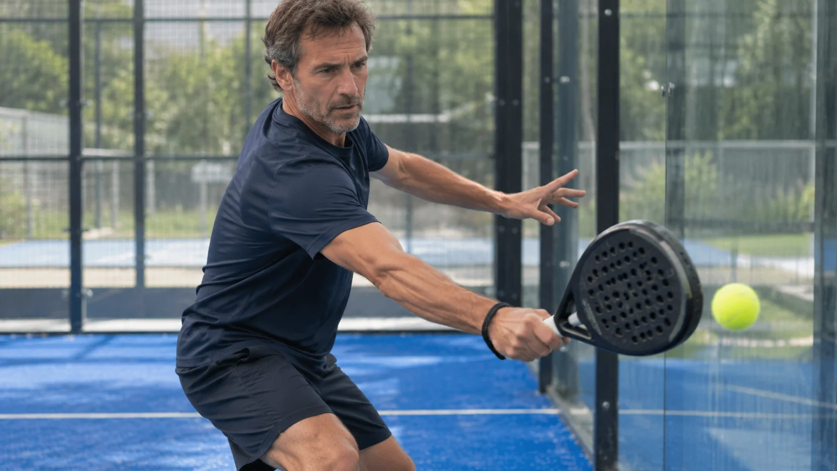 Padelspiller slår en baghånd ved glasvæggen, et slag der belaster senerne i albuen